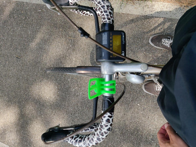 Photo of a bicycle showing sideways taken from the perspective of a person standing with the frame between their legs, standing slightly in front of the sattle. The picture shows the bike’s handlebar with a tape in a white, black and brown leopard-like pattern.